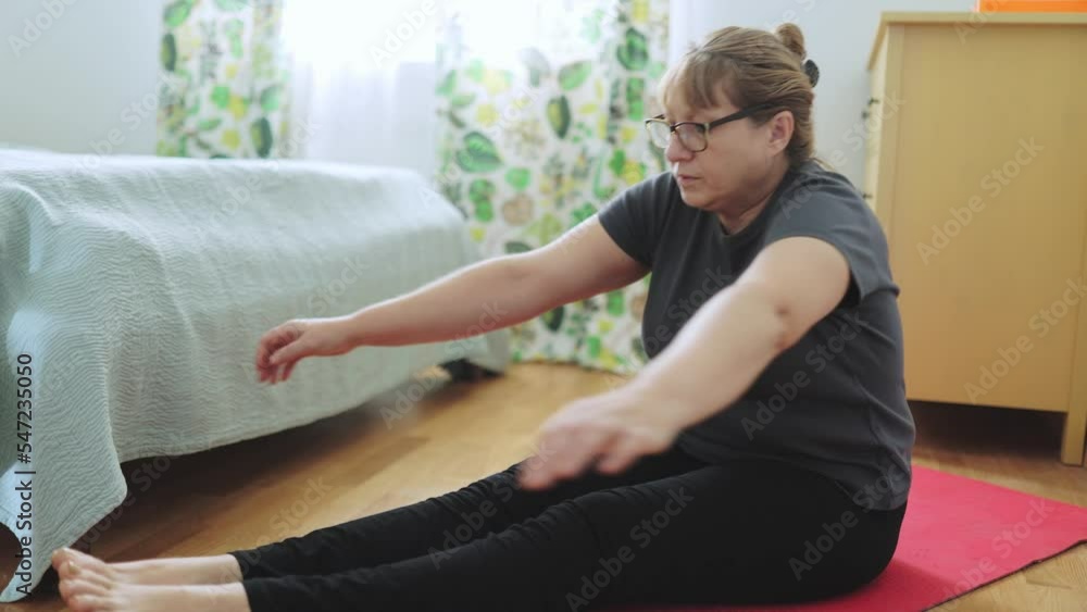 Active senior woman doing abs exercises on yoga mat at home and smiling at camera. Sporty mature lady working out in living room interior. Strength training concept Active senior woman doing abs exercises on yoga mat at home and smiling at camera. Sporty mature lady working out in living room interior. Strength training concept
