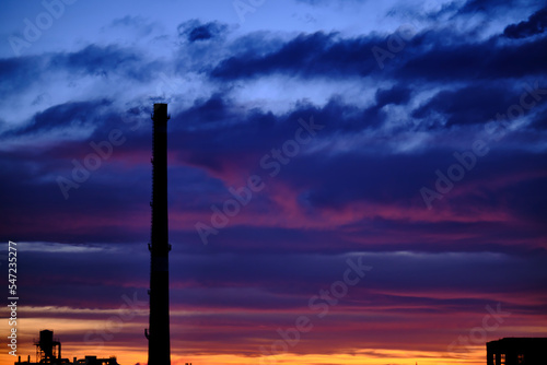 Silhouette of a factory with a large industrial pipe, against the background of an incredible sunset or sunrise sky © Aleksander