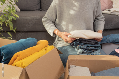 Woman sorting clothes and packing into cardboard box. Donations for charity, help low income families, declutter home, sell online, moving moving into new home, recycling, sustainable living concept