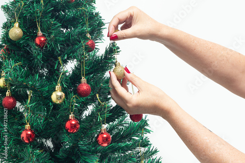 Mãos femininas com unhas pintadas de vermelho, segurando uma bola, montando a árvore de natal.