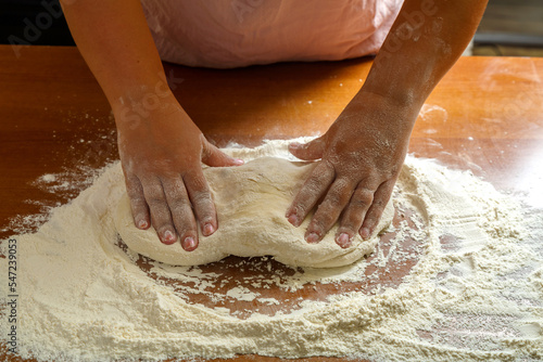 The hands of a Jewish woman knead the dough for challah for a festive meal on Shabbat on a wooden table.