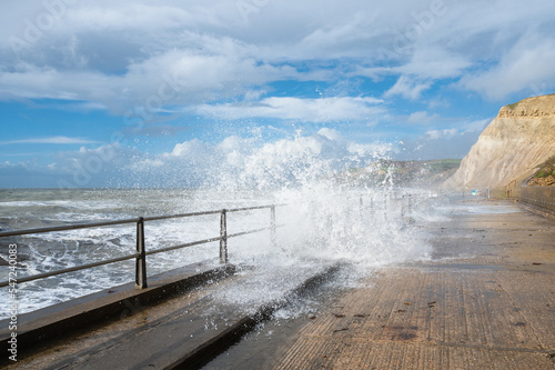 Big waves and water splashes at West Bay beach near Bridgport in Dorset, United Kingdom. Walkway or promenade along the beach, selective focus