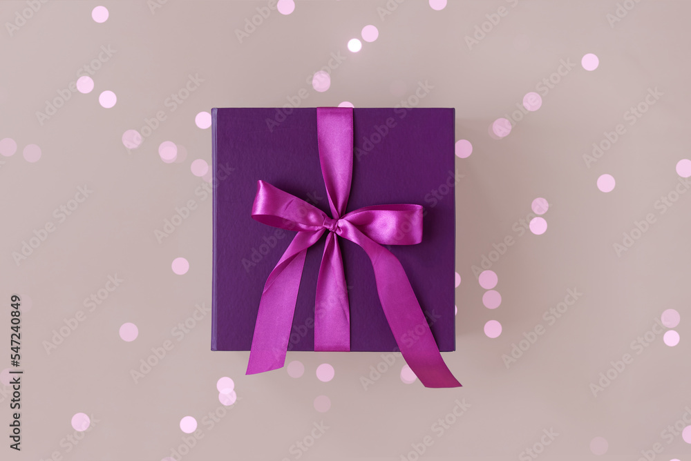 Violet gift box with a purple bow made of satin on soft beige background