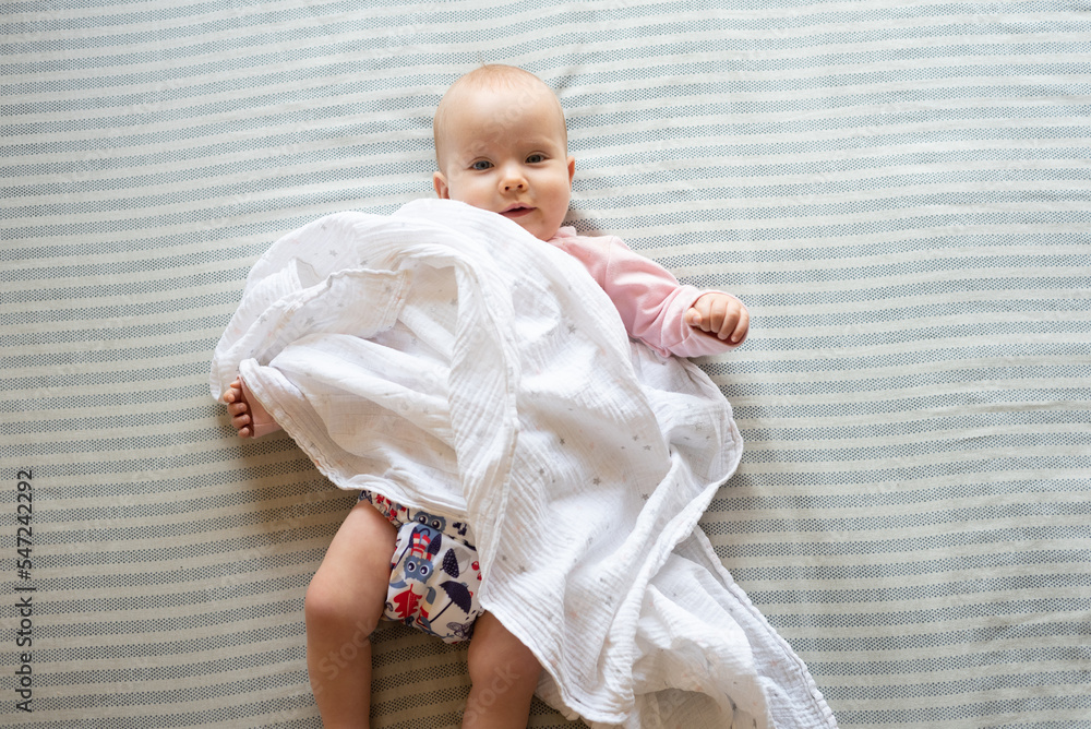 A happy and content baby girl lying on a bed. She is wearing a modern, reusable cloth diaper. A happy and content baby girl lying on a bed. She is wearing a modern, reusable cloth diaper.