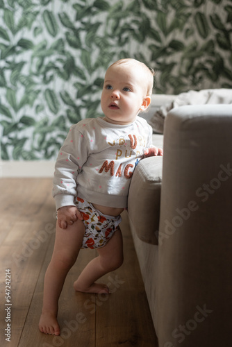 A baby girl learning how to stand up. She is wearing a modern, reusable cloth diaper