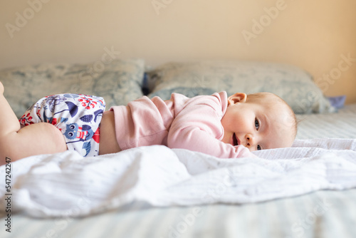 A happy, content baby lying on her stomach doing tummy time to strengthen her back. She is wearing a modern, reusable cloth diaper