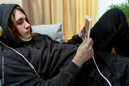Teenager who spends time lying on the sofa or in his bedroom consuming internet and social networks. Concept of internet and social media addiction. photo