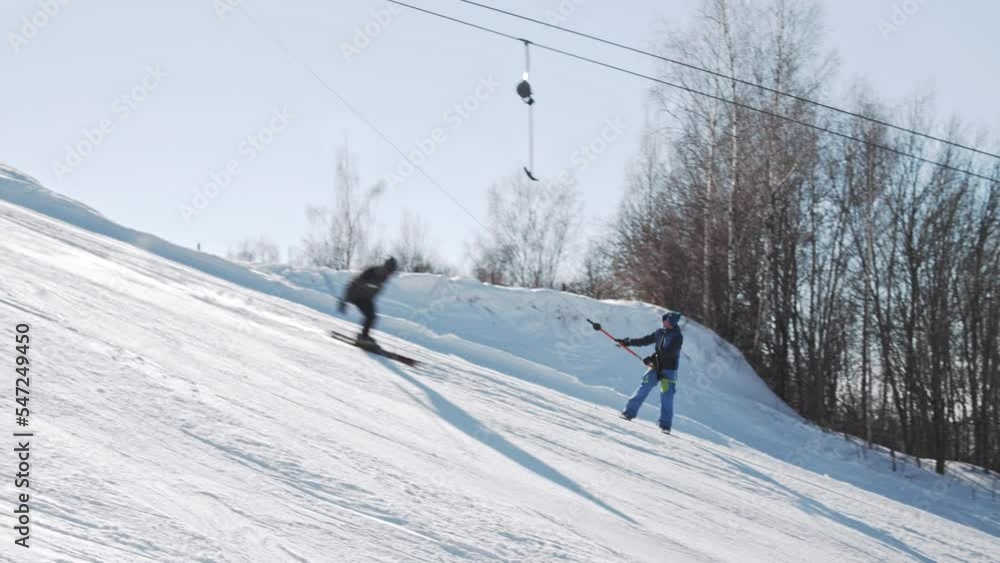A snowboarder climbs up on a hill using a T-bar lift on a sunny day at a ski resort and makes a buttering nose grab trick. Going up to the top of the slope on a tow lift. A snowboarder climbs up on a hill using a T-bar lift on a sunny day at a ski resort and makes a buttering nose grab trick. Going up to the top of the slope on a tow lift.