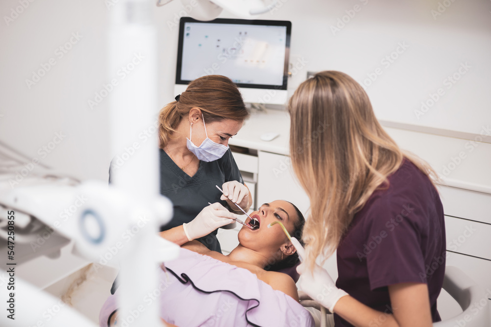 A female dentist and her assistant examine a patient's teeth in the dentist's chair.The hygienist uses an electrical device or an air turbine. Concept of mouth care, clean teeth.