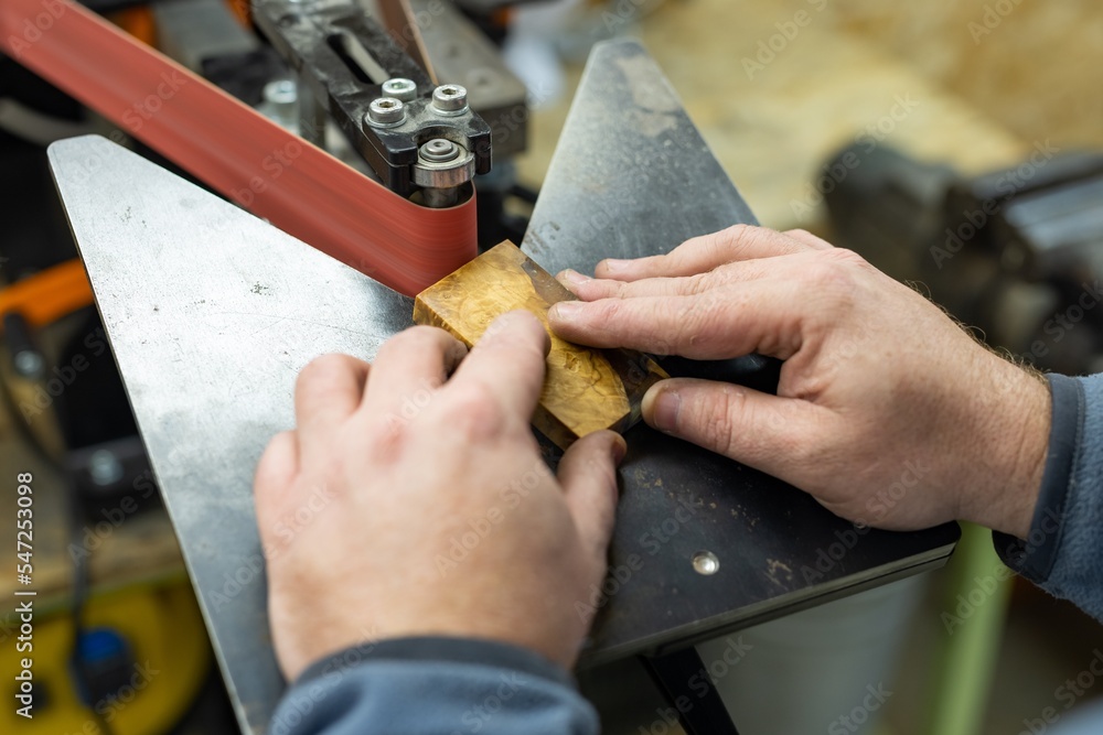 Industrial tool worker grinds a wood handle on a rotating belt sander