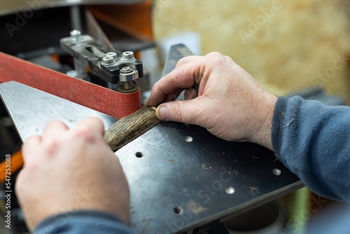 Industrial tool worker grinds a wood handle on a rotating belt sander, he makes a knife handle. photo