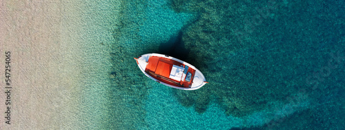 Aerial top view photo of colourful traditional wooden fishing boat anchored in Aegean island destination port with turquoise sea