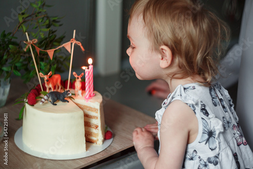A little girl celebrates her 3rd birthday, blows out the candles, in front of her is a cake with candles close-up.