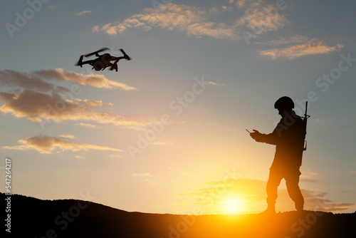 Silhouettes of soldiers are using drone and laptop computer for scouting during military operation against the backdrop of a sunset. Greeting card for Veterans Day, Memorial Day, Independence Day.