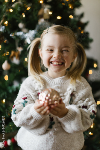 Little girl holding gold ornament in front of christmas tree