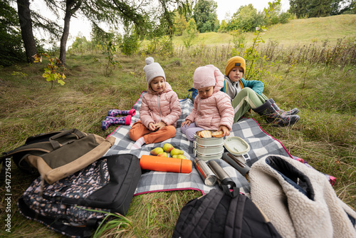 Picnic in autumn park. Three kids eat in the forest, while sitting on blanket.
