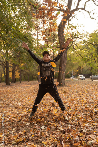 Happy teenage boy playing in the park  jumping and throwing a pile of yellow leaves  autumn mood 