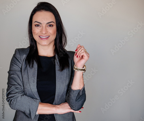 A mulher empreendedora em uma sessão de fotos corporativa em pose de pé sorridente vestida elegantemente com paletó e com mãos delicadas photo