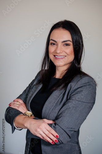 A mulher empreendedora em uma sessão de fotos corporativa em pose de pé sorridente vestida elegantemente com paletó e com braços cruzados