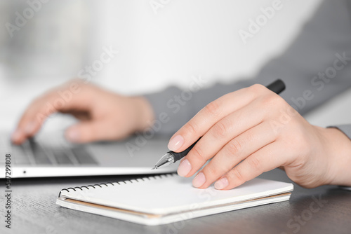 Woman with pen, laptop and notebook at wooden table, closeup. Electronic document management