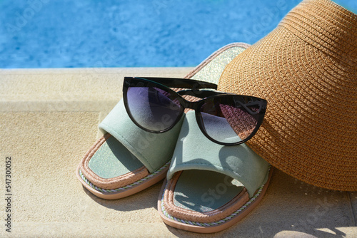 Stylish sunglasses, visor cap and slippers at poolside on sunny day. Beach accessories © New Africa