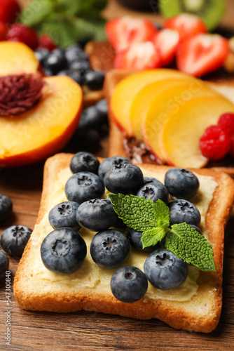 Tasty toast with butter, blueberry and mint on wooden table, closeup