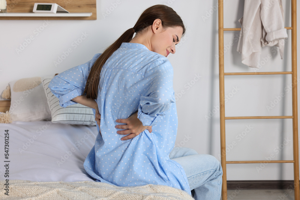Woman suffering from back pain while sitting on bed at home. Symptom of scoliosis Woman suffering from back pain while sitting on bed at home. Symptom of scoliosis