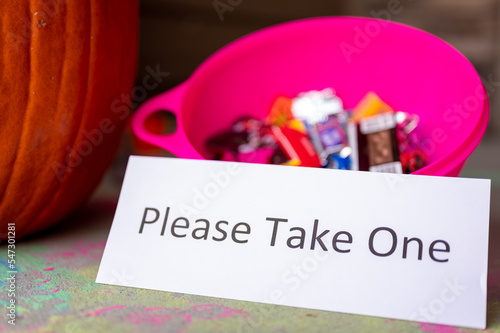 Bowl sitting on a doorway with a sign stating to please take one for Halloween trick or treaters.  photo