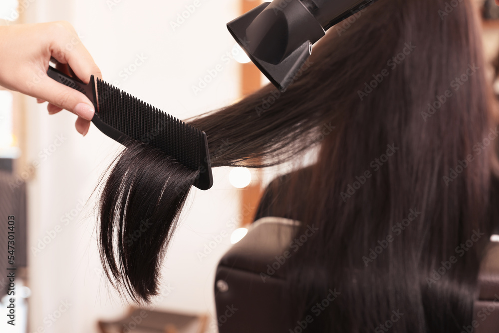 Fototapeta premium Hairdresser drying woman's hair in beauty salon, closeup