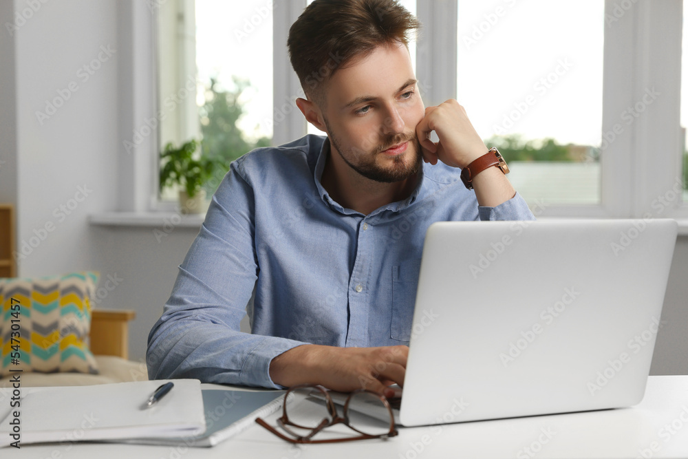 Handsome man working with laptop at table indoors Handsome man working with laptop at table indoors