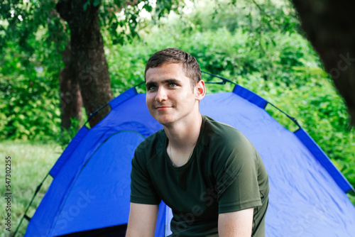 Defocus smiling young man tourist sitting in touristic tent at the beach. Camping, tourism and travel concept. Green forest. Out of focus