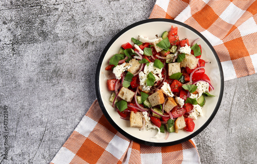 Tuscan Panzanella, traditional Italian salad with tomatoes and bread. Vegetarian panzanella salad on a round plate on a dark gray background. Top view, flat lay