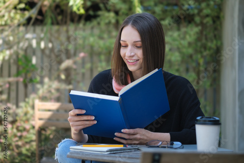 Pleased young woman in warm sweater relaxing outdoor and reading book.