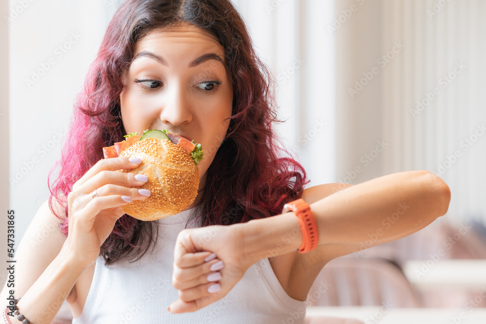 The girl was in a hurry looking at wristwatch and finishing to eat her burger in a fast food cafe