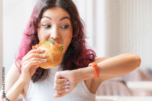 Obraz na płótnie The girl was in a hurry looking at wristwatch and finishing to eat her burger in a fast food cafe w salonie