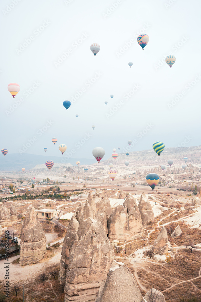 Stunning view some hot air balloons flying over the beautiful Cappadocia landscape during a cloudy day. Goreme, central Antolia, Turkey.
