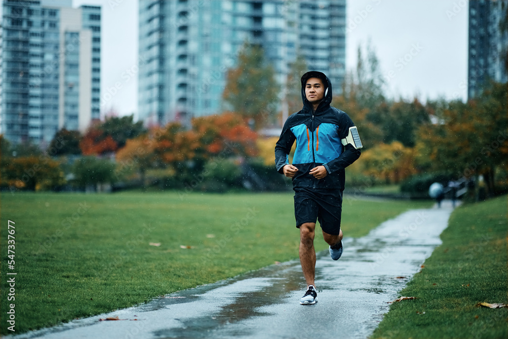 Athletic man running in park during rainy day.