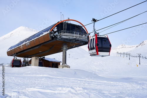 Cable car gondola at ski resort with snowy mountains on background. Modern ski lift with funitels and supporting towers high in the mountains on winter day. Ski lift station with no people. photo
