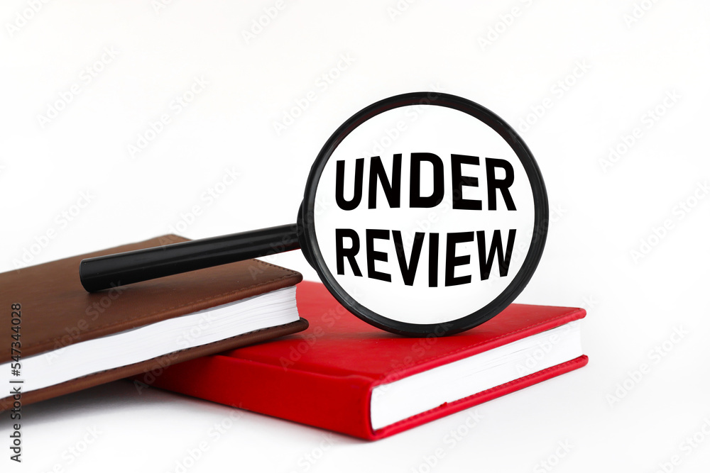 under review text on glass magnifier lies on two notebooks on the table under review text on glass magnifier lies on two notebooks on the table