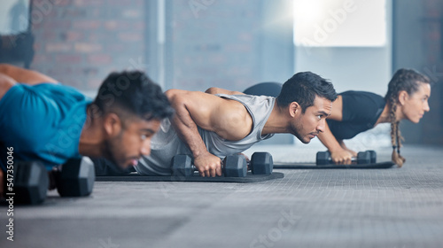 Fitness, exercise and gym with a personal trainer teaching or training a class workout in a health club. Motivation, coach and dumbbells with a man athlete and student group in a session for strength