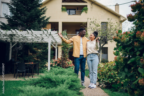 Фотография Multiracial couple holding keys and standing outside their new home