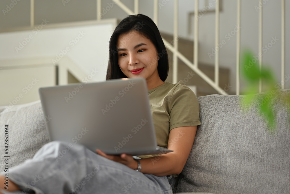 Millennial Asian woman using laptop while sitting on sofa, Shopping online, Chatting in social network, Watching movie or Working. Millennial Asian woman using laptop while sitting on sofa, Shopping online, Chatting in social network, Watching movie or Working.