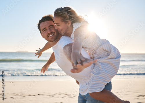 Happy, couple and piggyback walk on the beach for love, travel or summer vacation bonding together in the outdoors. Man carrying woman on back with smile enjoying playful fun time walking by the sea #547353018