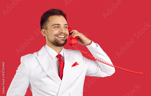Φωτογραφία Smiling man in suit isolated on red studio background talk on landline phone