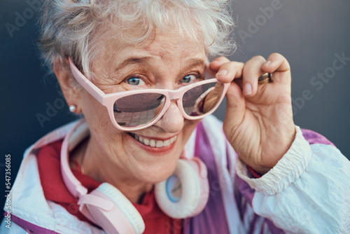 Face portrait and senior woman with sunglasses, headphones and vintage clothing. Fashion, beauty and happy, retired and elderly female in retro, cool and pink designer glasses and outfit with smile.