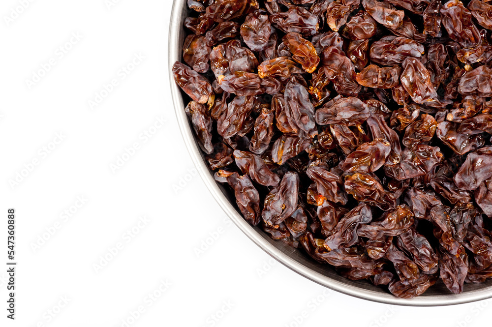 Dark-colored raisins lying in a metal container, shot on a white background. Dark-colored raisins lying in a metal container, shot on a white background.