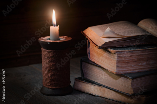 reading books concept, vintage style, a stack of old books and a lit candle on a wooden desk