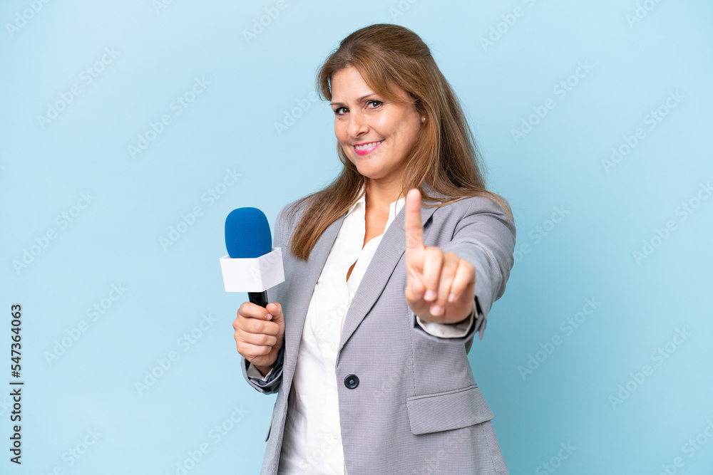 Middle-aged TV presenter woman over isolated blue background showing and lifting a finger Middle-aged TV presenter woman over isolated blue background showing and lifting a finger