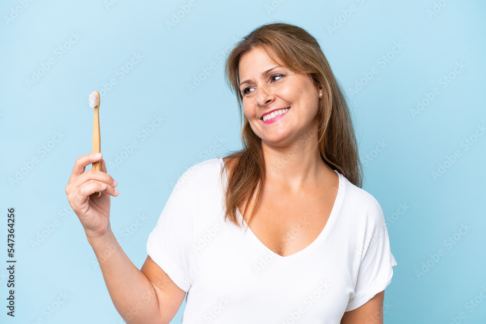Middle-aged caucasian woman brushing teeth isolated on blue background with happy expression Middle-aged caucasian woman brushing teeth isolated on blue background with happy expression