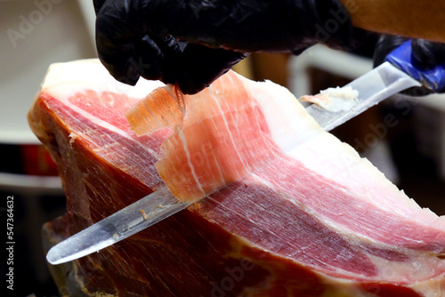 Photos gloved hand of the butcher who slices a slice of raw ham with a sharp knife